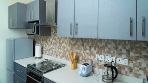 A kitchen with grey cabinets, a gas stove, a toaster, and a coffee maker. - Modern 2-Bedroom Apartment Home on a Gated Compound with Backup Solar Power. (Amrahia)