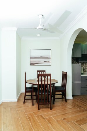 A dining area with a round table and four chairs, a ceiling fan, and a kitchen visible through an archway. - Modern 2-Bedroom Apartment Home on a Gated Compound with Backup Solar Power. (Amrahia)