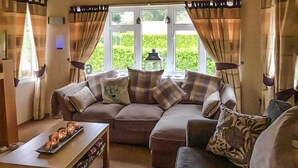A cozy living room with a sectional sofa, a coffee table, and a view of greenery outside. - Gorgeous (sta)caravan in Tzummarum (Tzummarum)