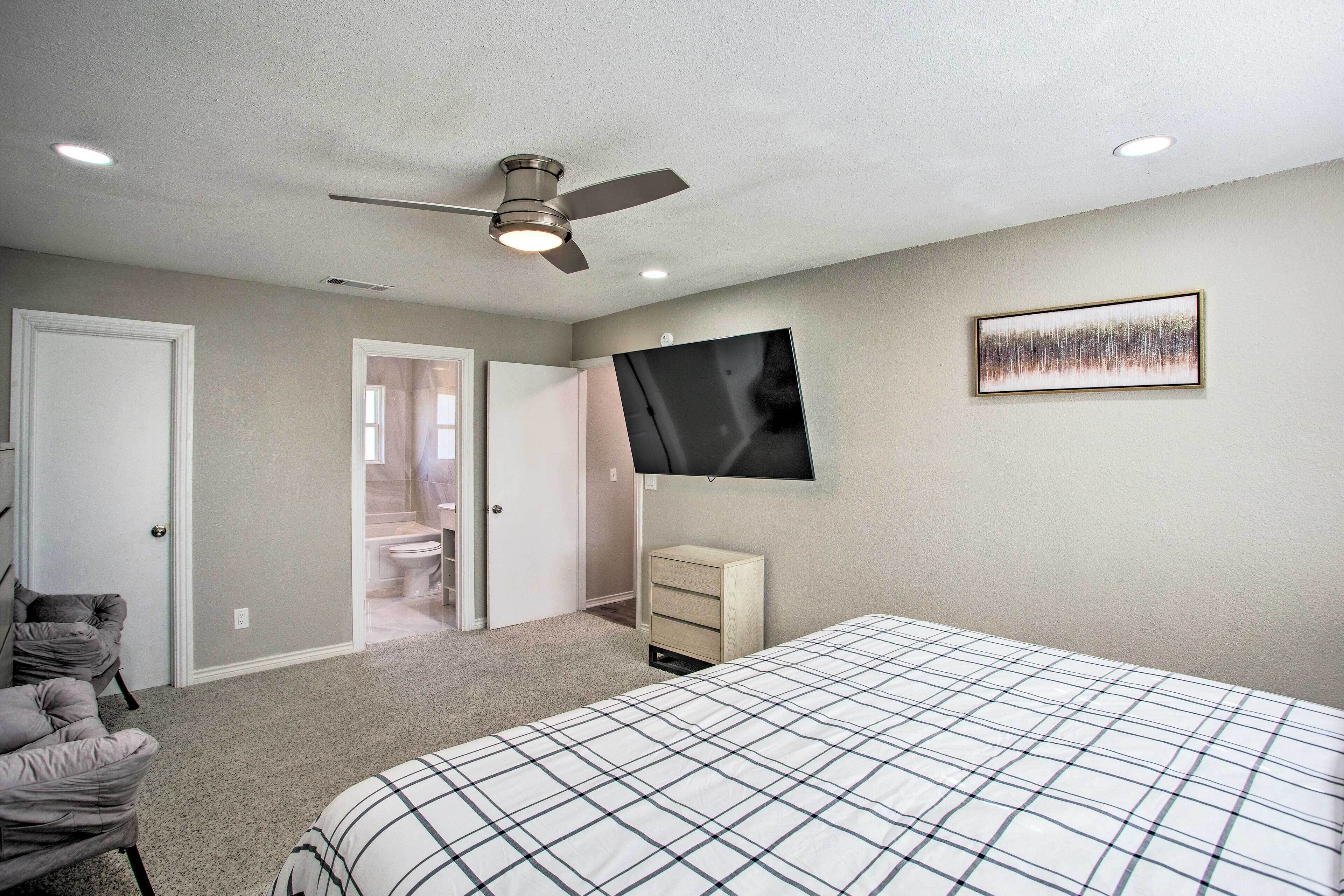 A bedroom with a bed, a ceiling fan, a TV mounted on the wall, and a door leading to a bathroom.