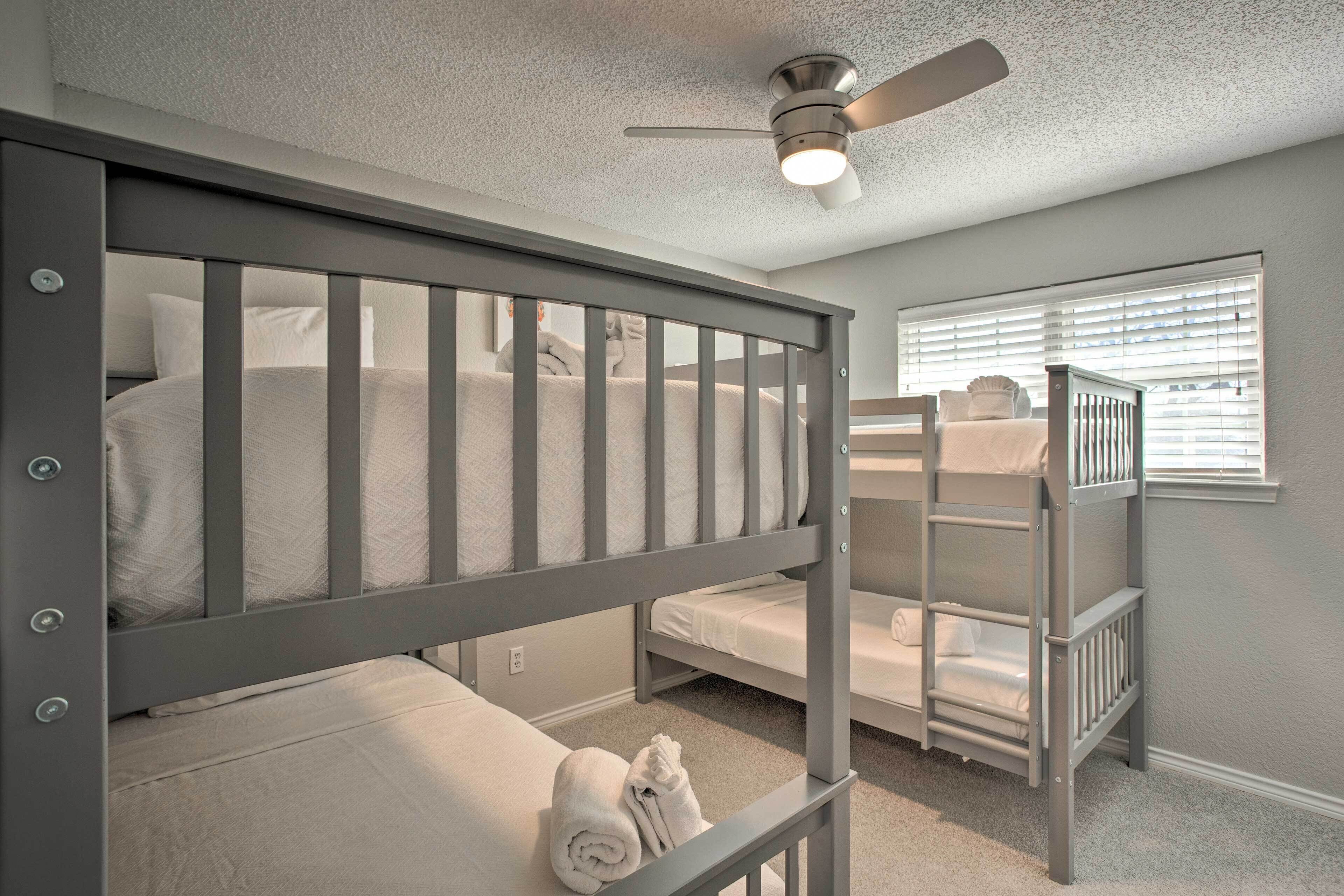A room with bunk beds, a ceiling fan, and a window with blinds.