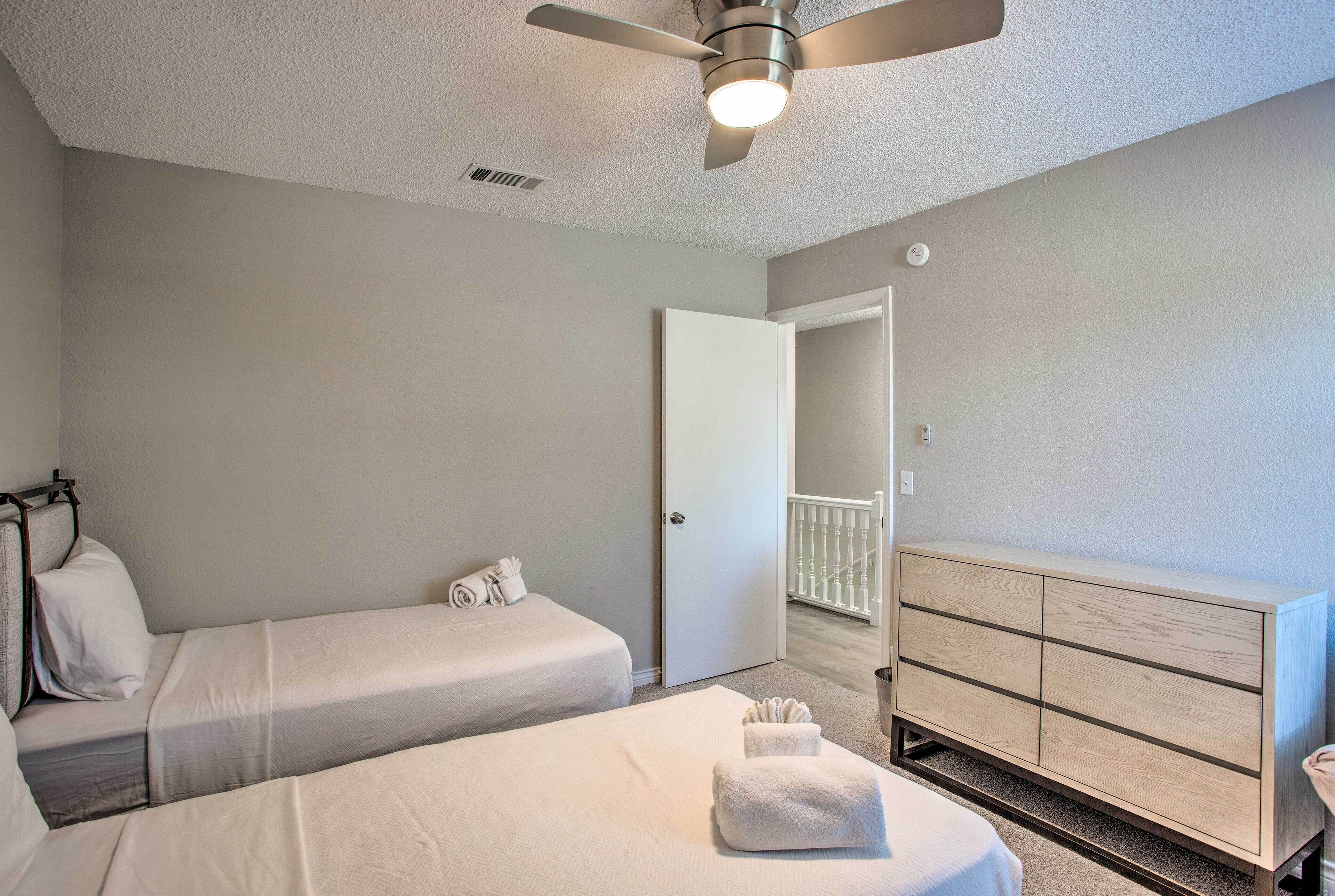 A hotel room with two single beds, a wooden dresser, a ceiling fan, and a door leading to a balcony.