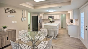 A modern kitchen with white cabinets, a central island, and a dining area with white chairs. - Richardson Home w/ Pool, Hot Tub & Arcade Games (Richardson)