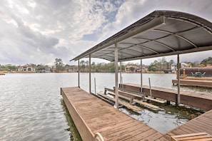 A wooden dock with a covered seating area, extending over a calm body of water.