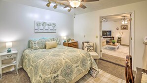 A bedroom with a bed, nightstands, a ceiling fan, a wall-mounted lamp, and a door leading to a living area. - Akron Apartment w/ Balcony - Hunting Nearby! (Akron)