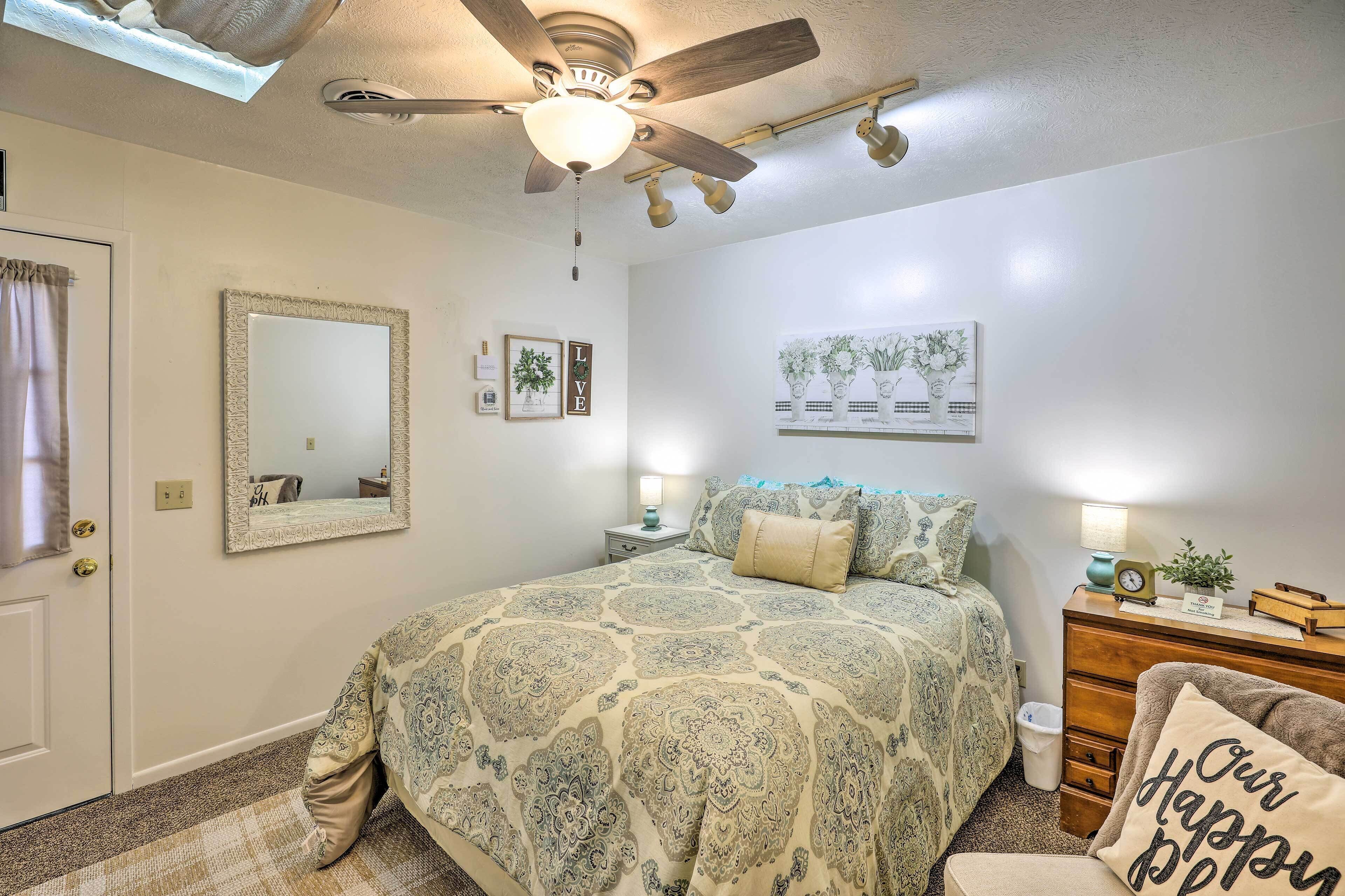 A bedroom with a bed, a ceiling fan, a dresser, a mirror, and wall decorations.