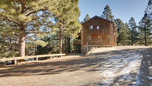 A two-story wooden cabin with a balcony, surrounded by pine trees and a gravel driveway. - The Bridgeway Casita - Apt Near Natl Parks (Duck Creek Village)