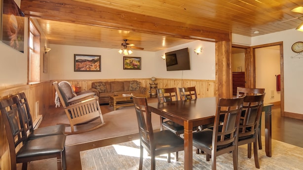 A dining area with wooden tables and chairs, a ceiling fan, and wall-mounted lights. - The Bridgeway Casita - Apt Near Natl Parks (Duck Creek Village)