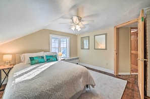 A bedroom with a large bed, a ceiling fan, a window, and a door.