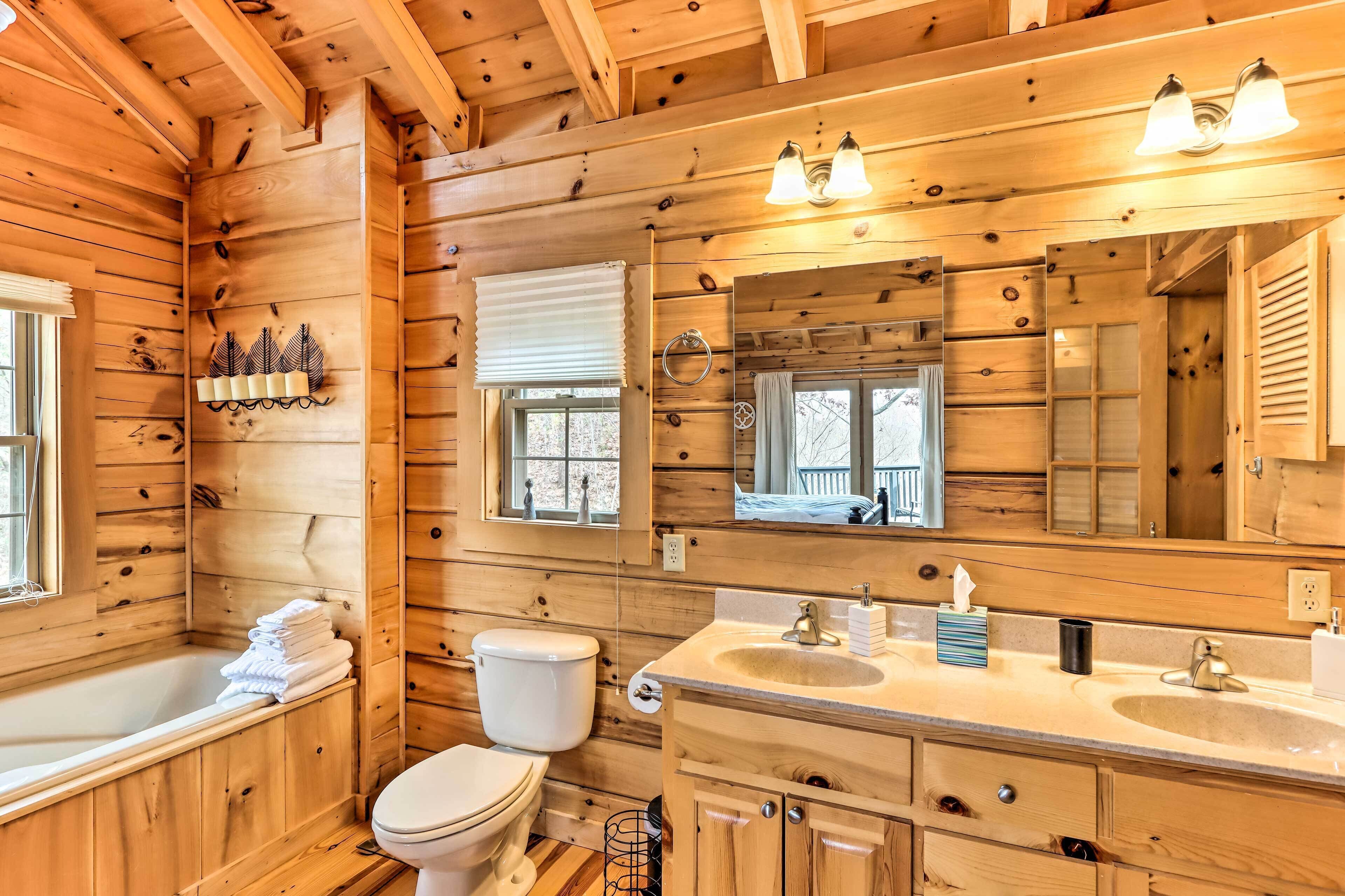 A wooden cabin bathroom with a bathtub, toilet, and two sinks.