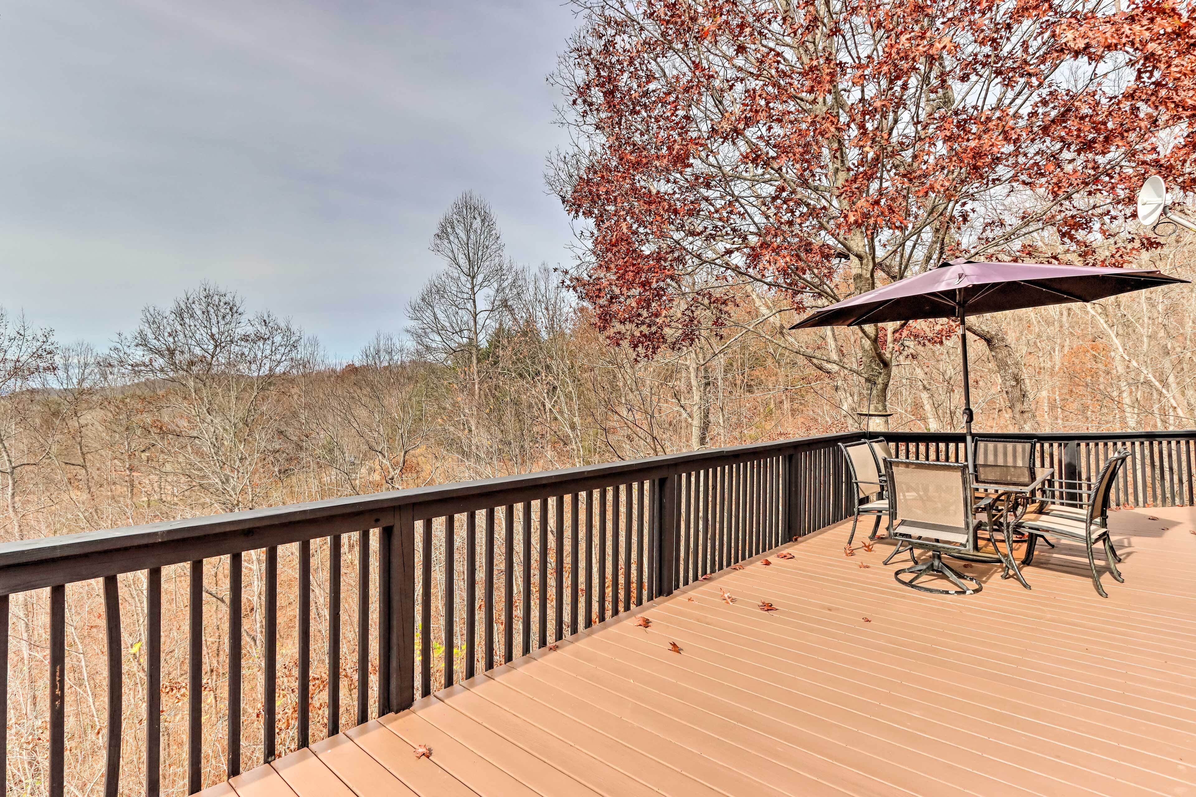 Une terrasse en bois avec une table et des chaises, un parasol et une vue sur les arbres et les collines.
