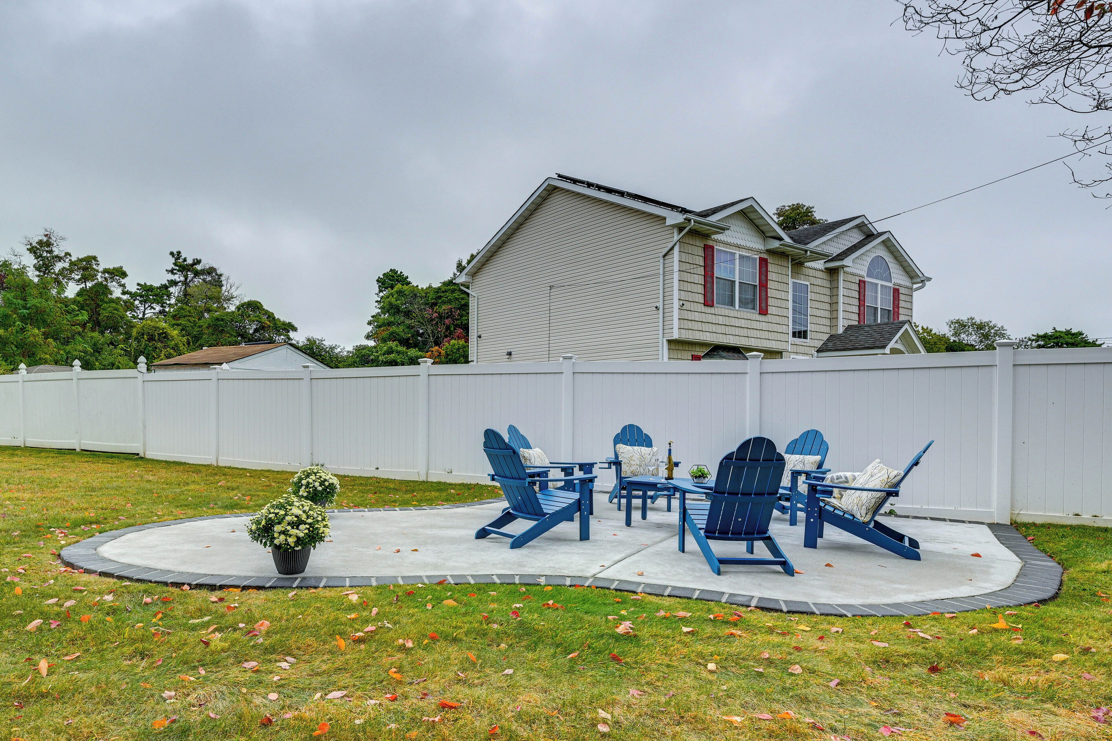 A backyard with a patio area featuring blue Adirondack chairs and a small table.