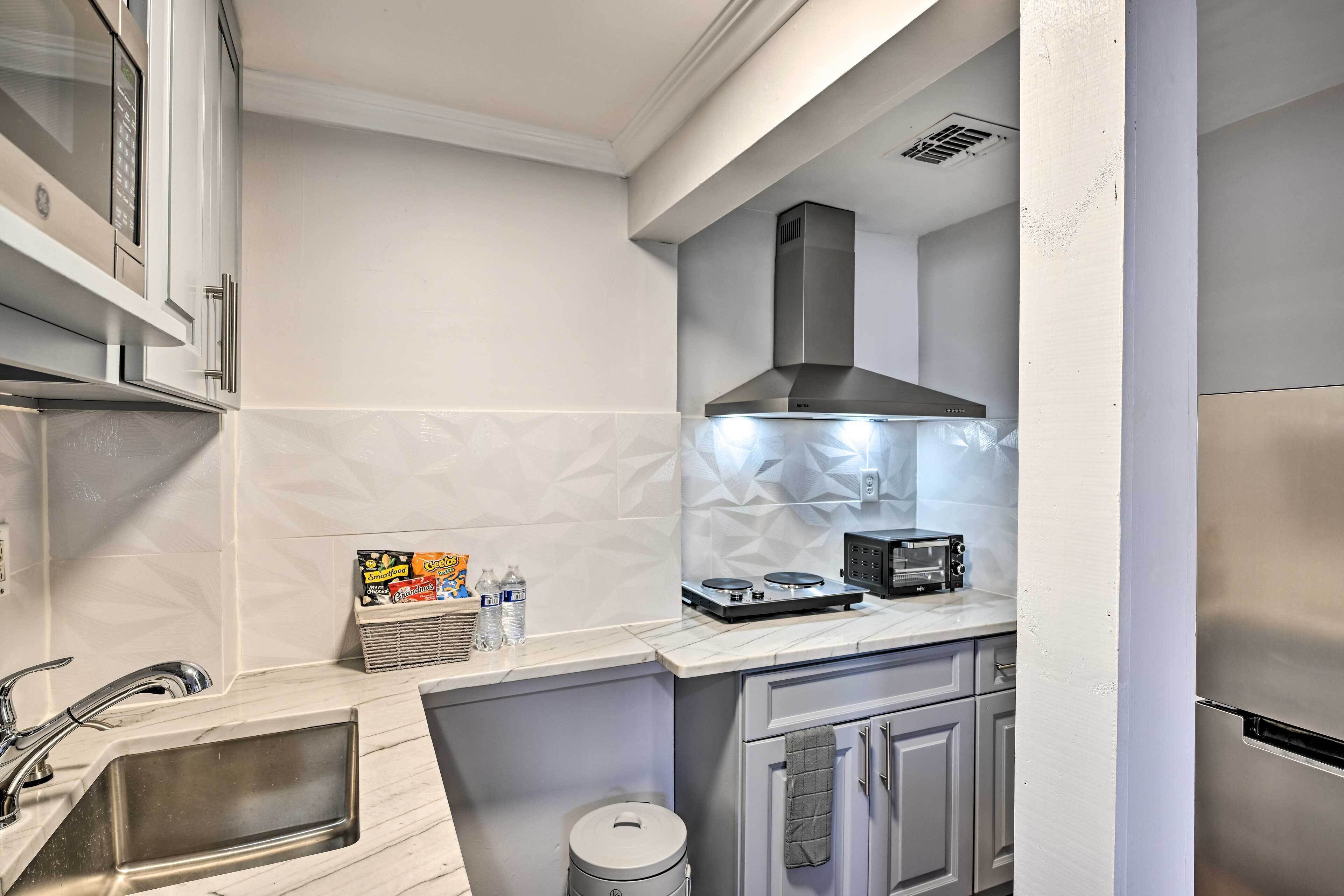 A modern kitchen with a stainless steel refrigerator, a built-in oven, and a microwave. There is a sink with a faucet, a countertop with a toaster, and a trash can.