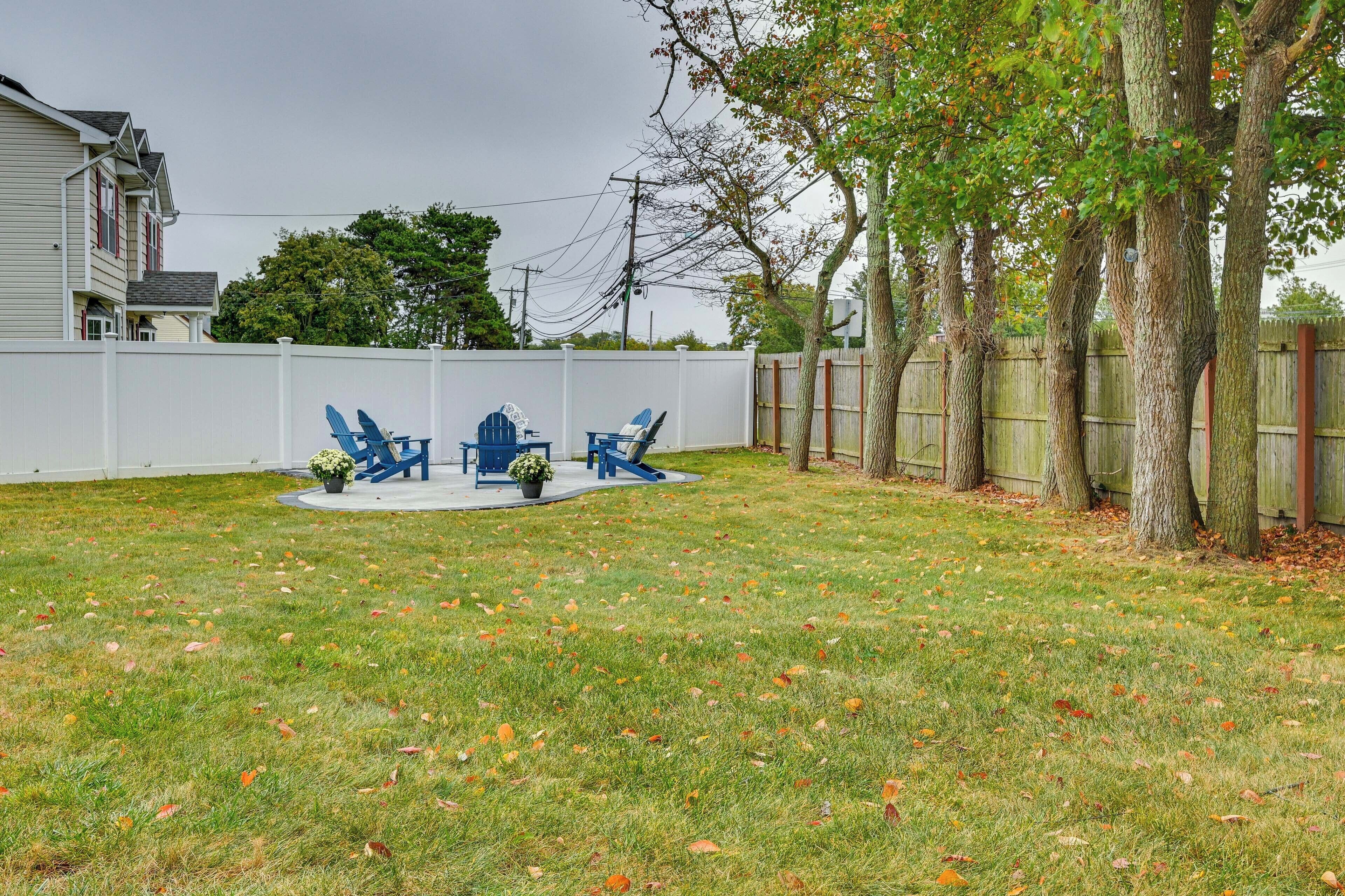 A backyard with a white fence, a wooden deck, and a lawn with scattered leaves.