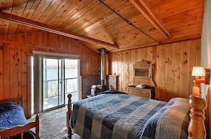 A wooden cabin bedroom with a large bed, a window, and a fireplace. - Bayfront Hancock Cottage w/ Beach Access & Views! (Hancock)