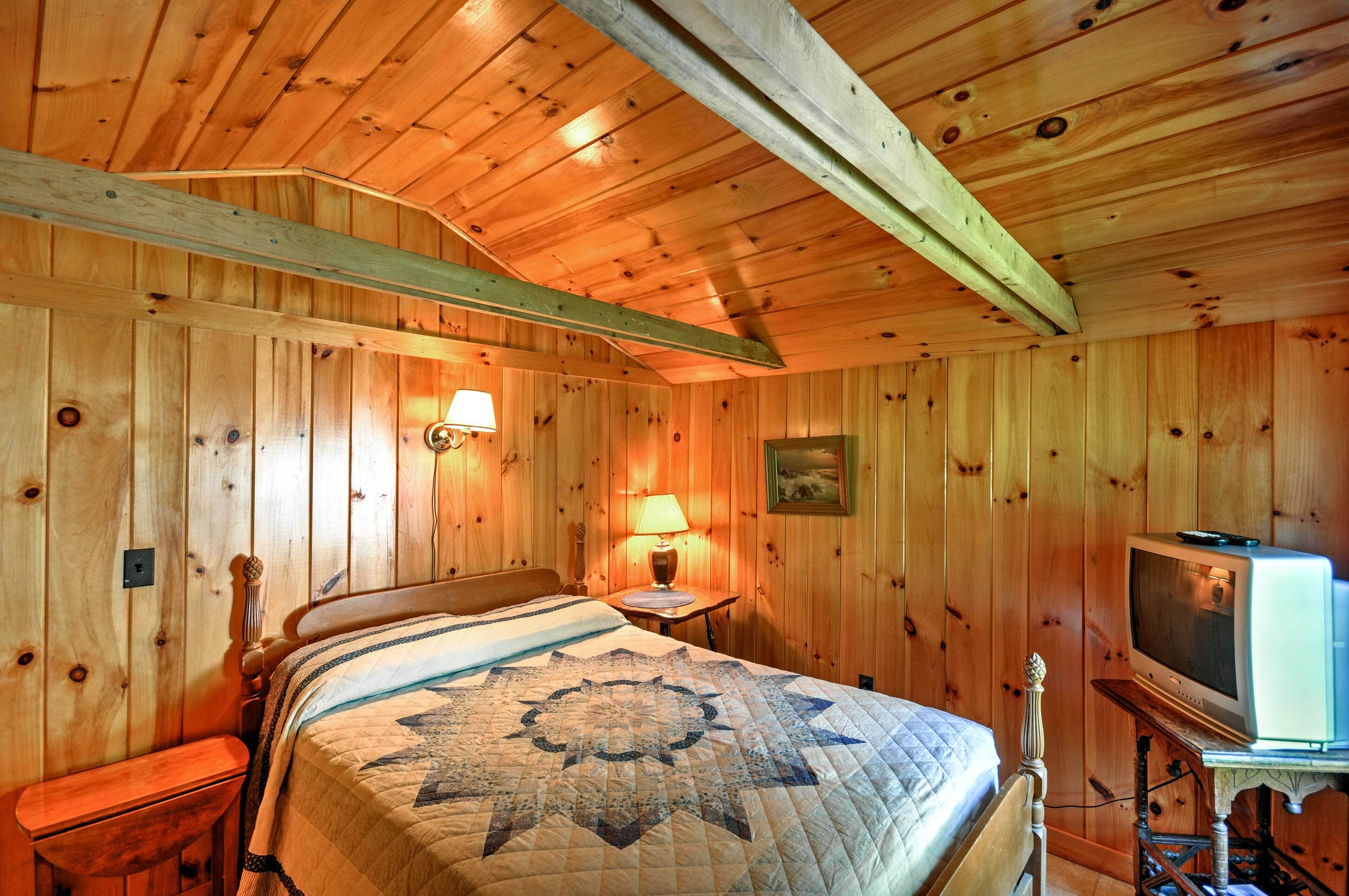 Een kamer met houten lambrisering, een bed, nachtkastje, lamp en een televisie.