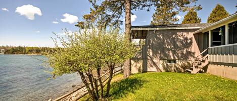 A lakeside cabin with a grassy yard, a wooden deck, and a stone pathway leading to the water.