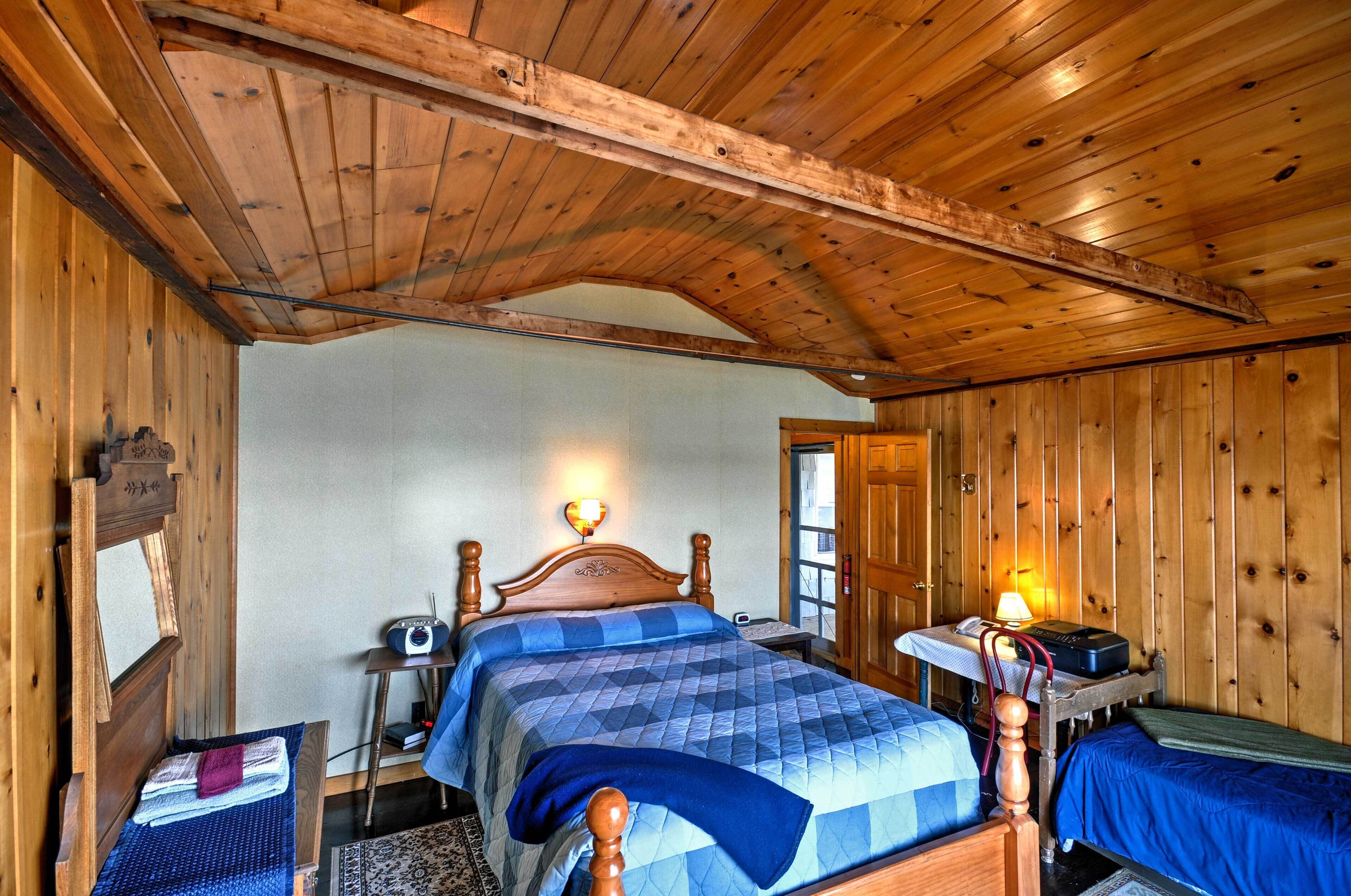 Ein Zimmer mit Holzwänden, einem Bett, einem Nachttisch mit Lampe und einem kleinen Tisch mit Radio.