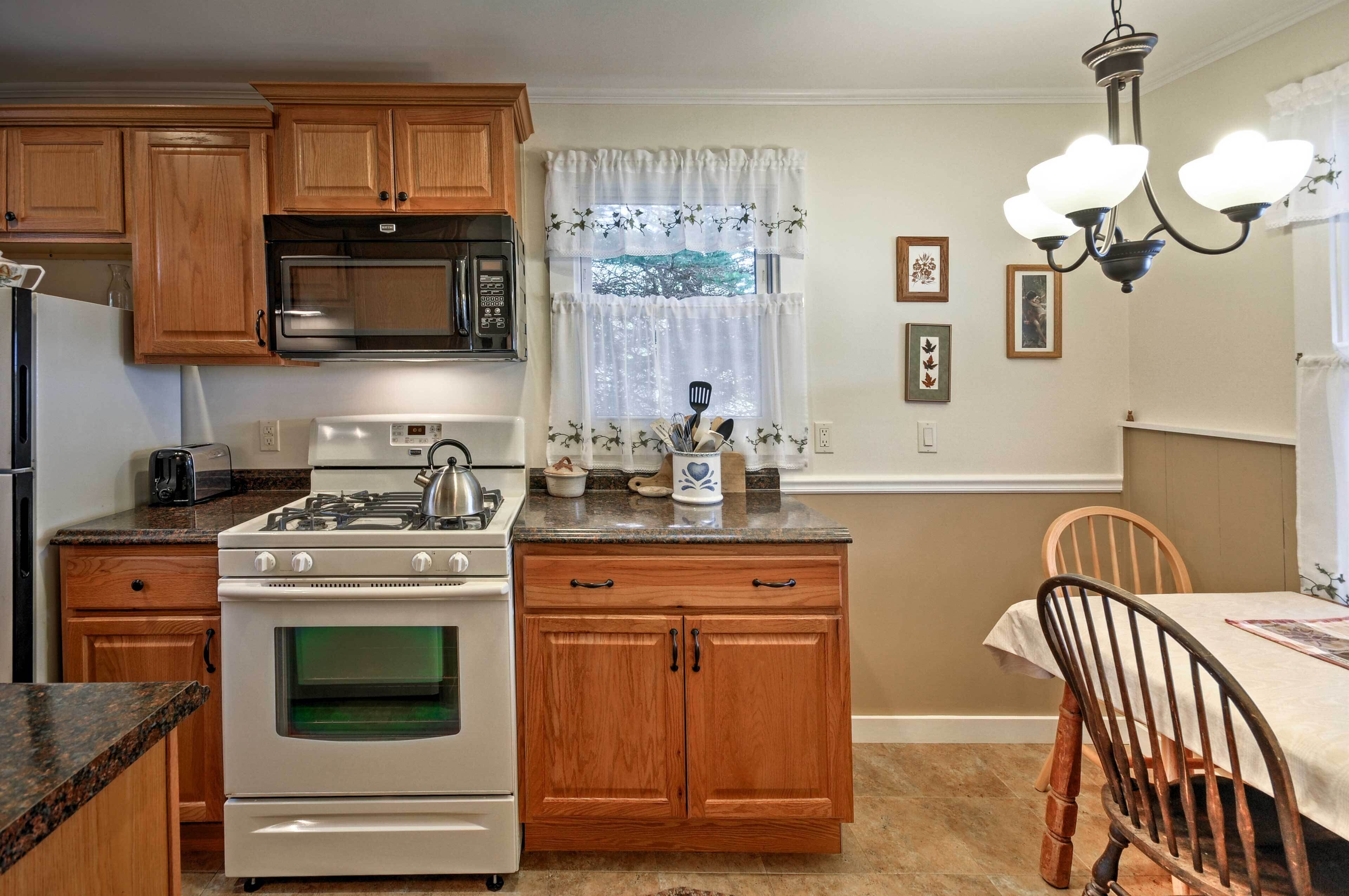 A kitchen with wooden cabinets, a stove, a microwave, and a dining area with a table and chairs.