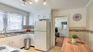 A kitchen with white cabinets, a stainless steel sink, a refrigerator, and a wooden dining table.