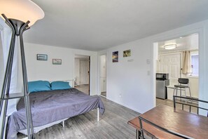 Een slaapkamer met een bed, nachtkastje en een moderne lamp. Er is een keukenhoek met een magnetron en een koelkast.