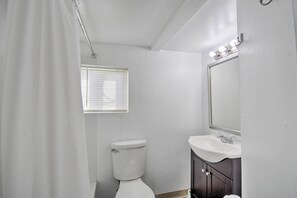 Een badkamer met toilet, wastafel, spiegel en een raam met zonwering.
