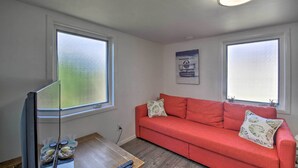 A living room with a red sofa, two windows, a ceiling light, and a wooden table with a remote control.