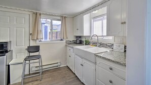 A compact kitchen with white cabinets, a granite countertop, a sink, a chair, and a microwave.