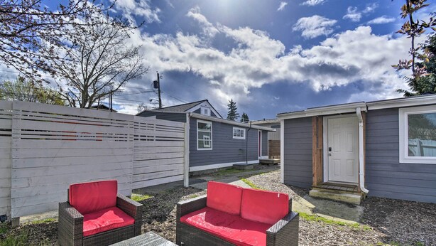 A backyard with wicker furniture and a small table, a wooden fence, and a house with a door and windows.