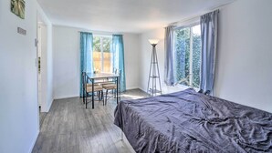 A room with a bed, a desk, and a chair. There is a window with curtains, a floor lamp, and a door.