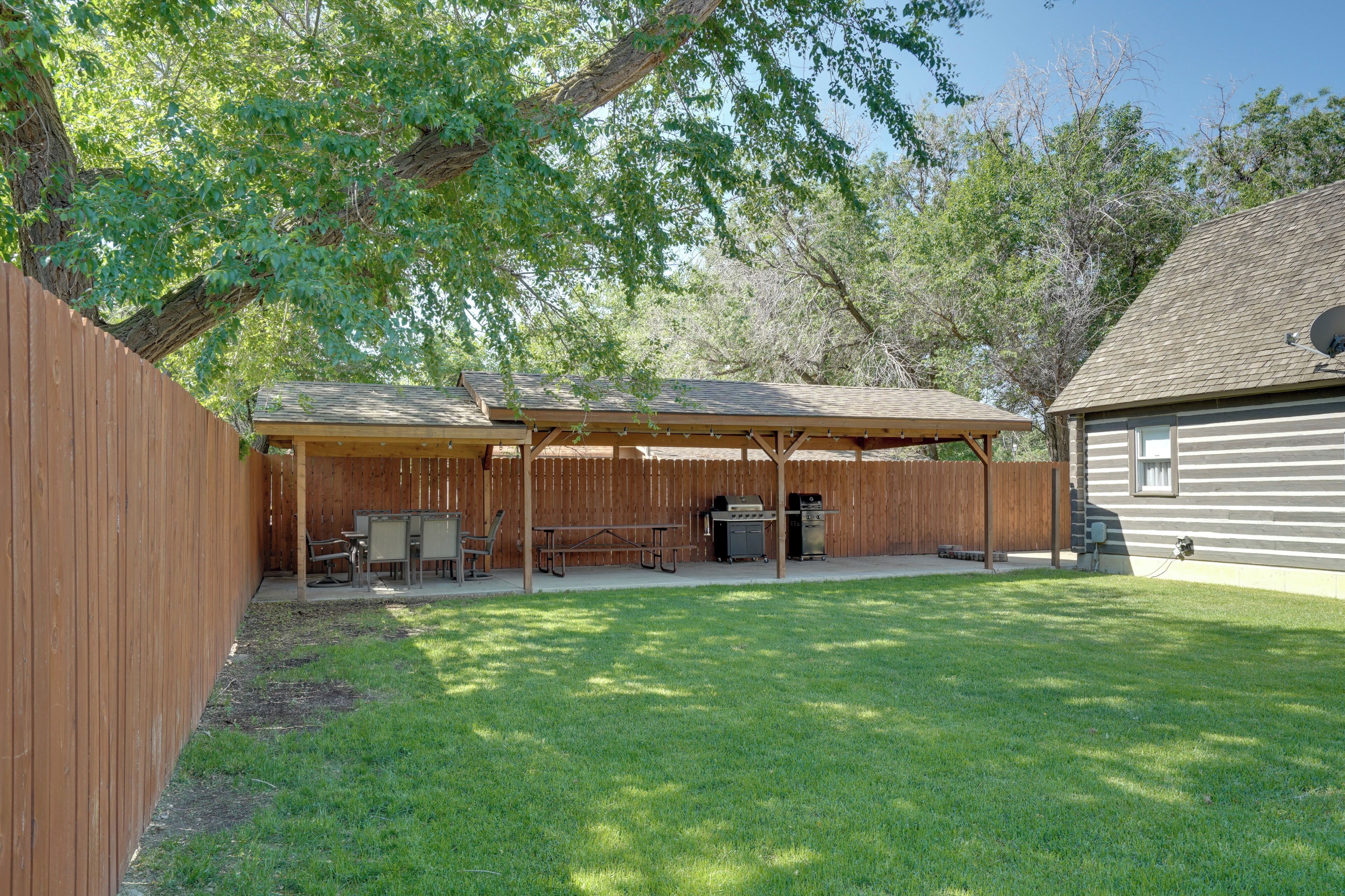 A backyard with a wooden deck, picnic table, grill, and a house in the background.