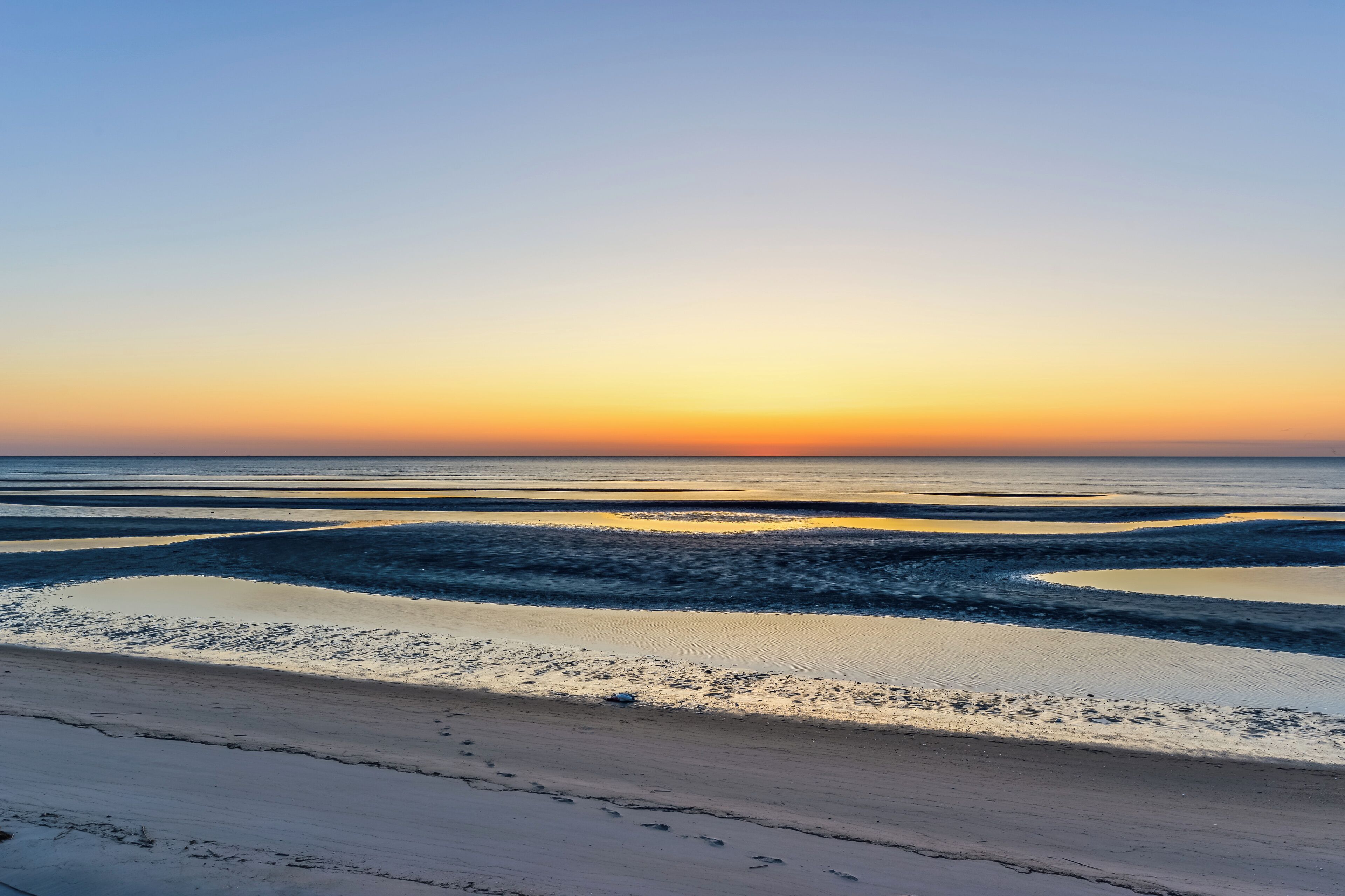 A beach with a calm sea and a clear sky at sunset.