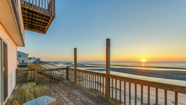 A wooden deck with a table and chairs, overlooking a beach with a sunset. - Private Beach Access! Bayfront Cape May Cottage (Cape May Court House)