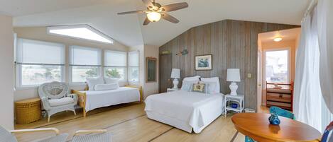 A bedroom with a bed, two chairs, a table, a ceiling fan, and a window with blinds.