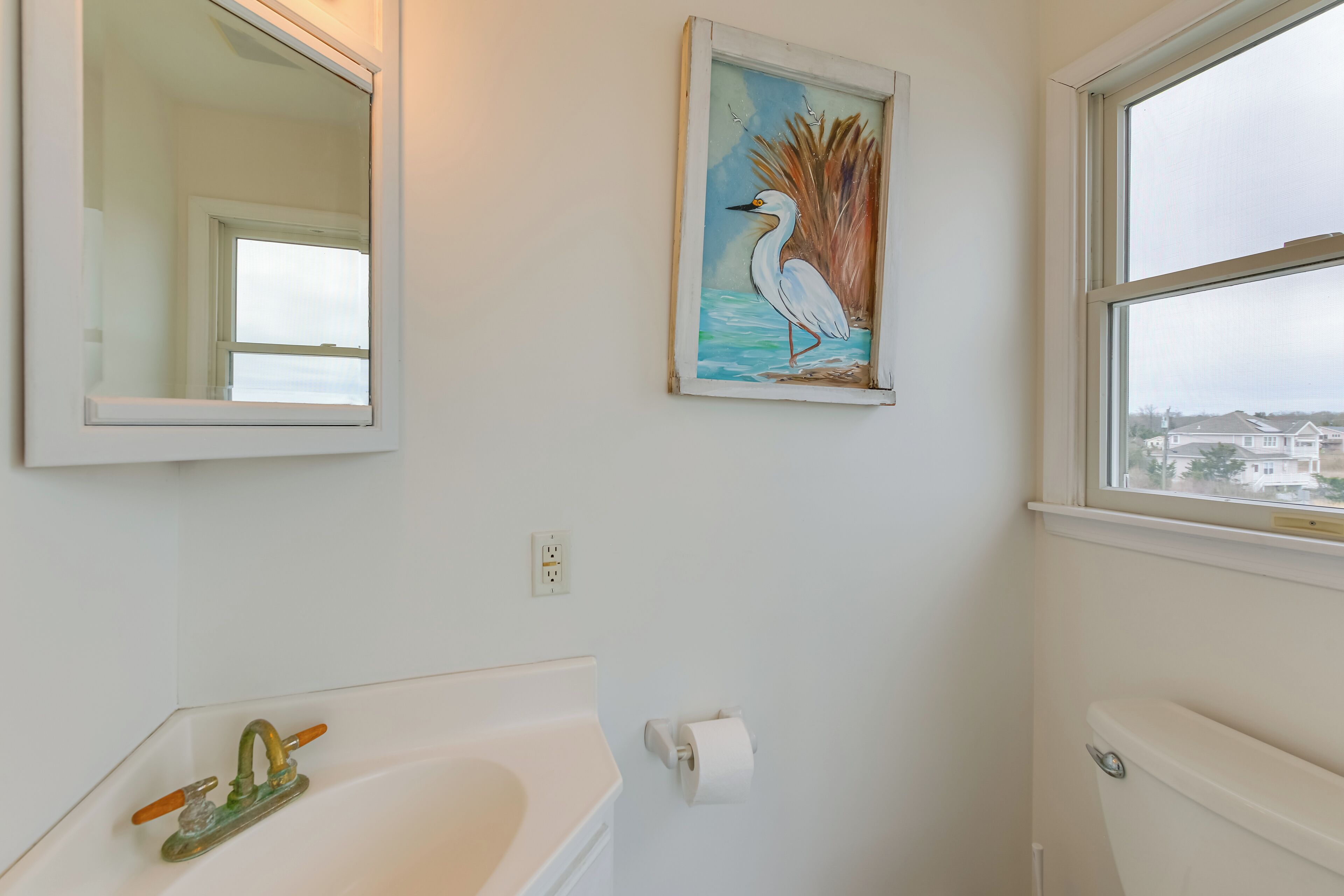 A bathroom with a white bathtub, a mirror, a toilet, and a painting of a bird.