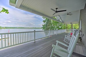 Eine überdachte Terrasse mit weißen Geländern, Deckenventilatoren und Schaukelstühlen mit Blick auf einen See.