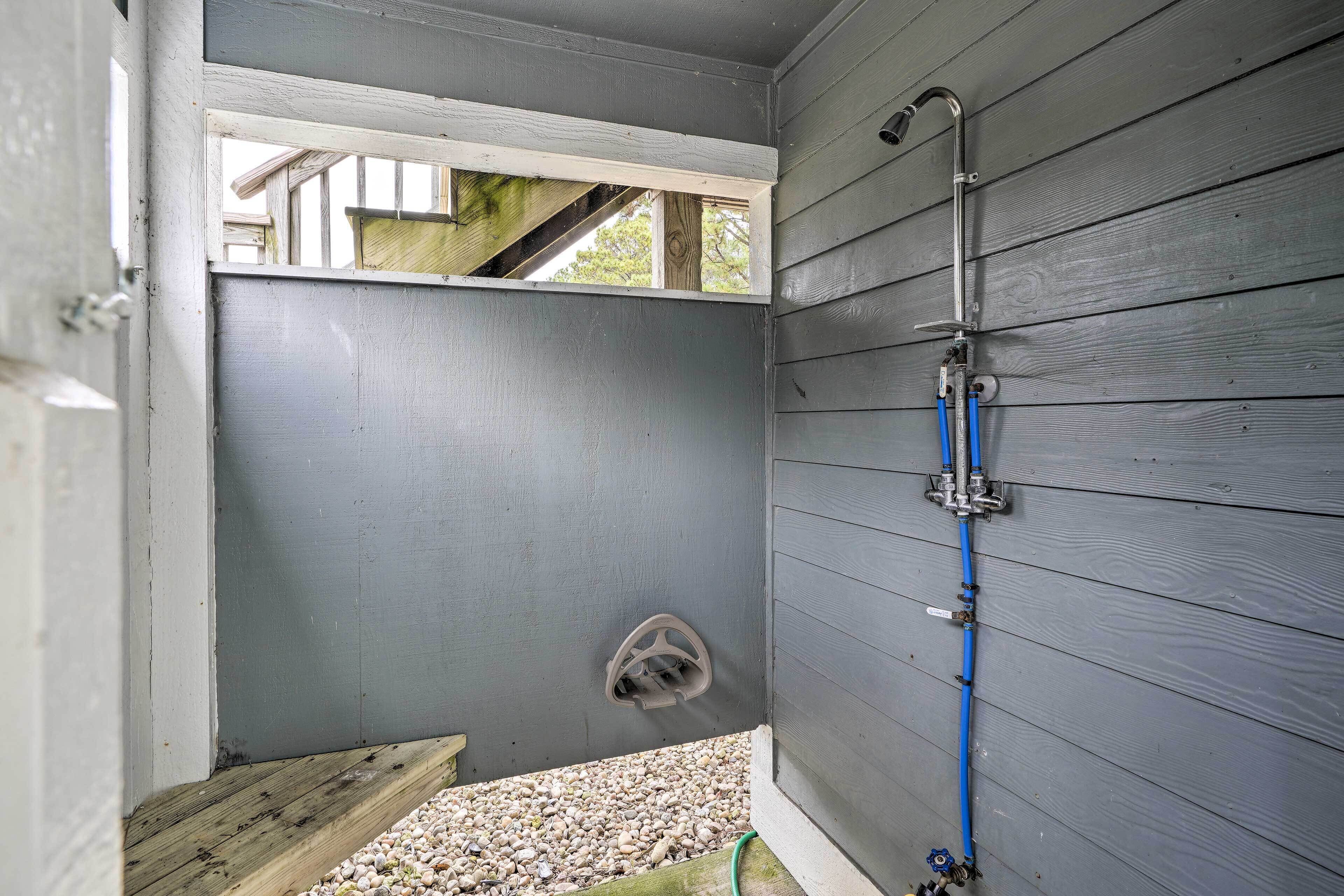 A small, enclosed shower area with a wooden bench, a window, and a blue pipe running along the wall.