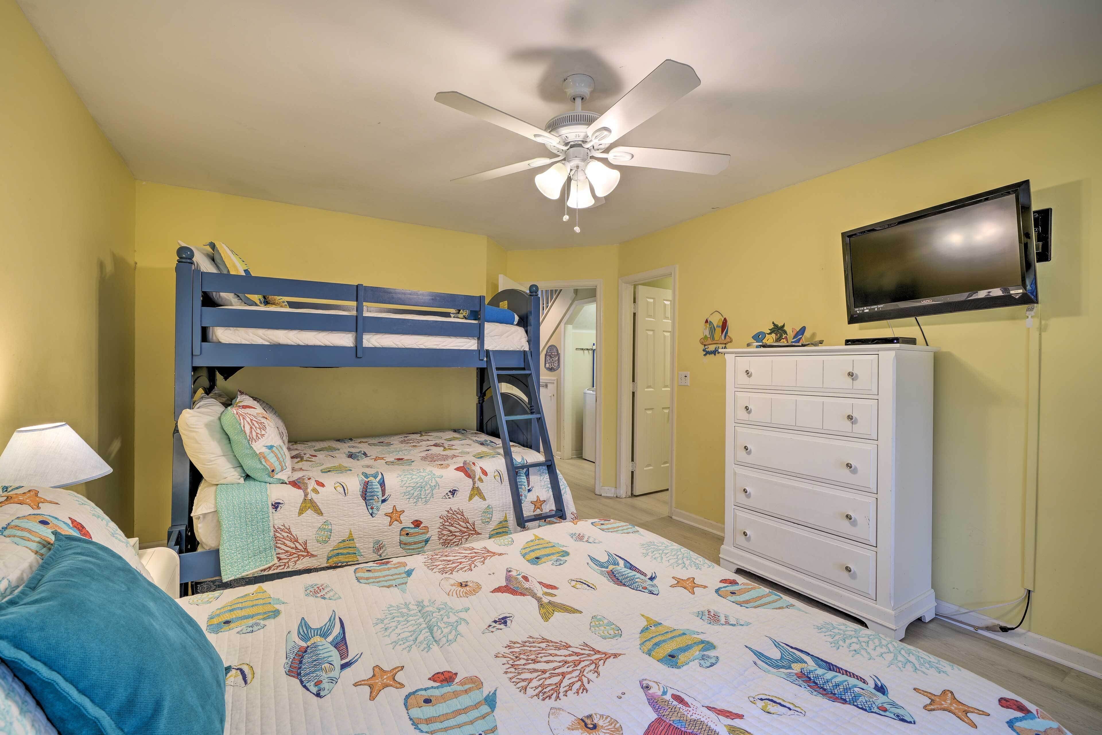 A bedroom with bunk beds, a ceiling fan, a television, and a dresser.
