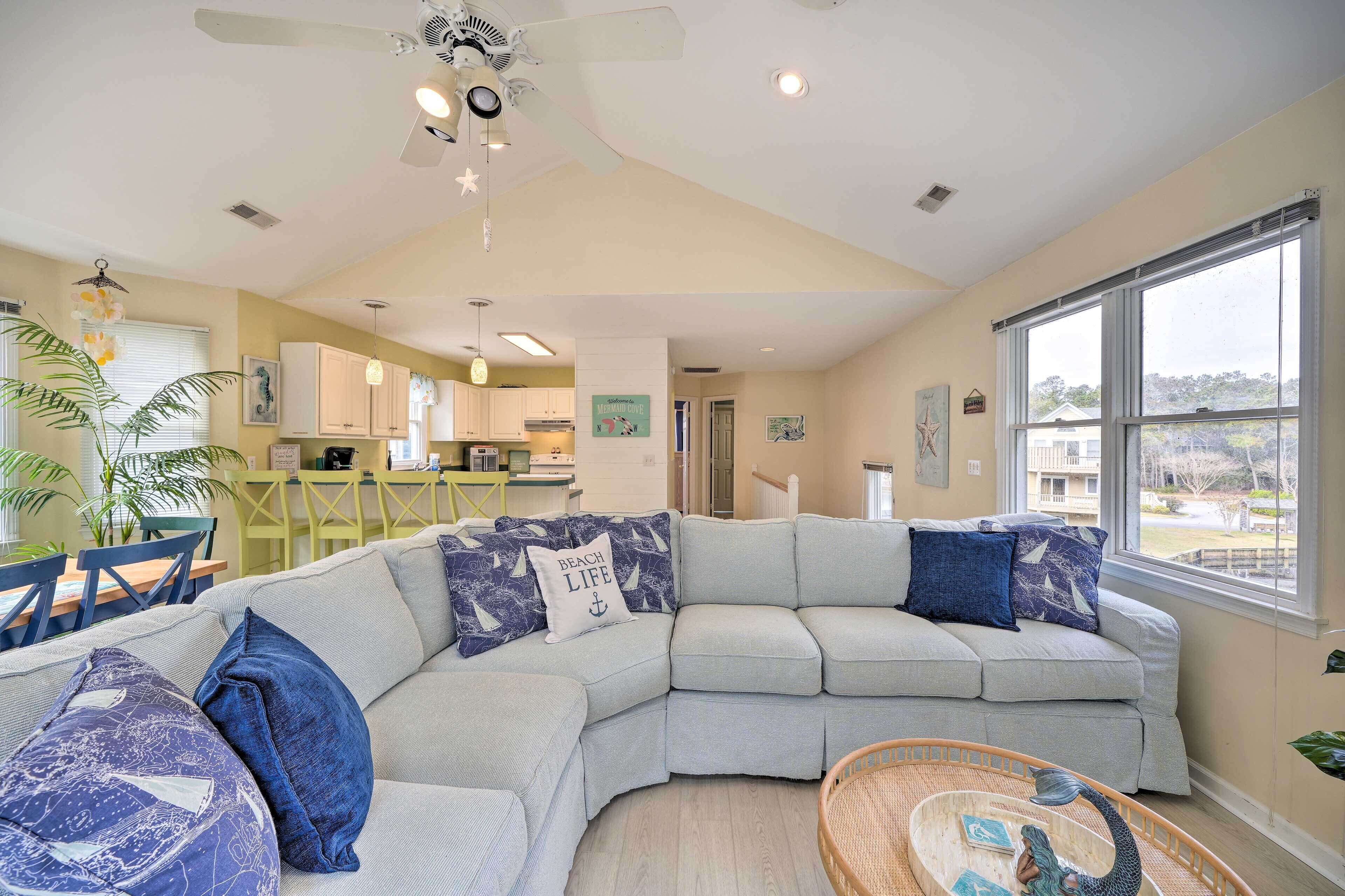 A spacious living area with a large L-shaped sofa, a ceiling fan, and a view of the kitchen and dining area.