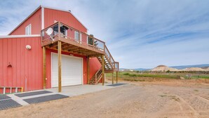 Une grange rouge avec un escalier en bois menant à un balcon, une porte de garage blanche et une allée en terre.