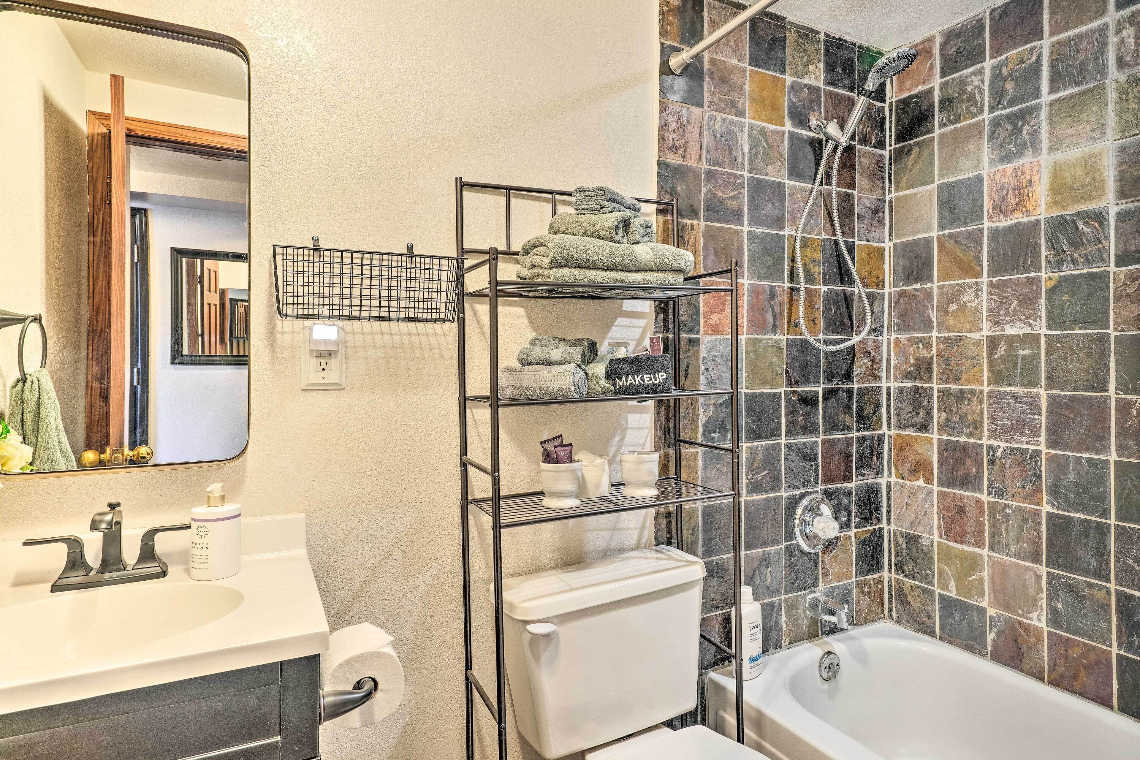 A bathroom with a white sink, a toilet, a shower with a rain showerhead, and a tiled wall.