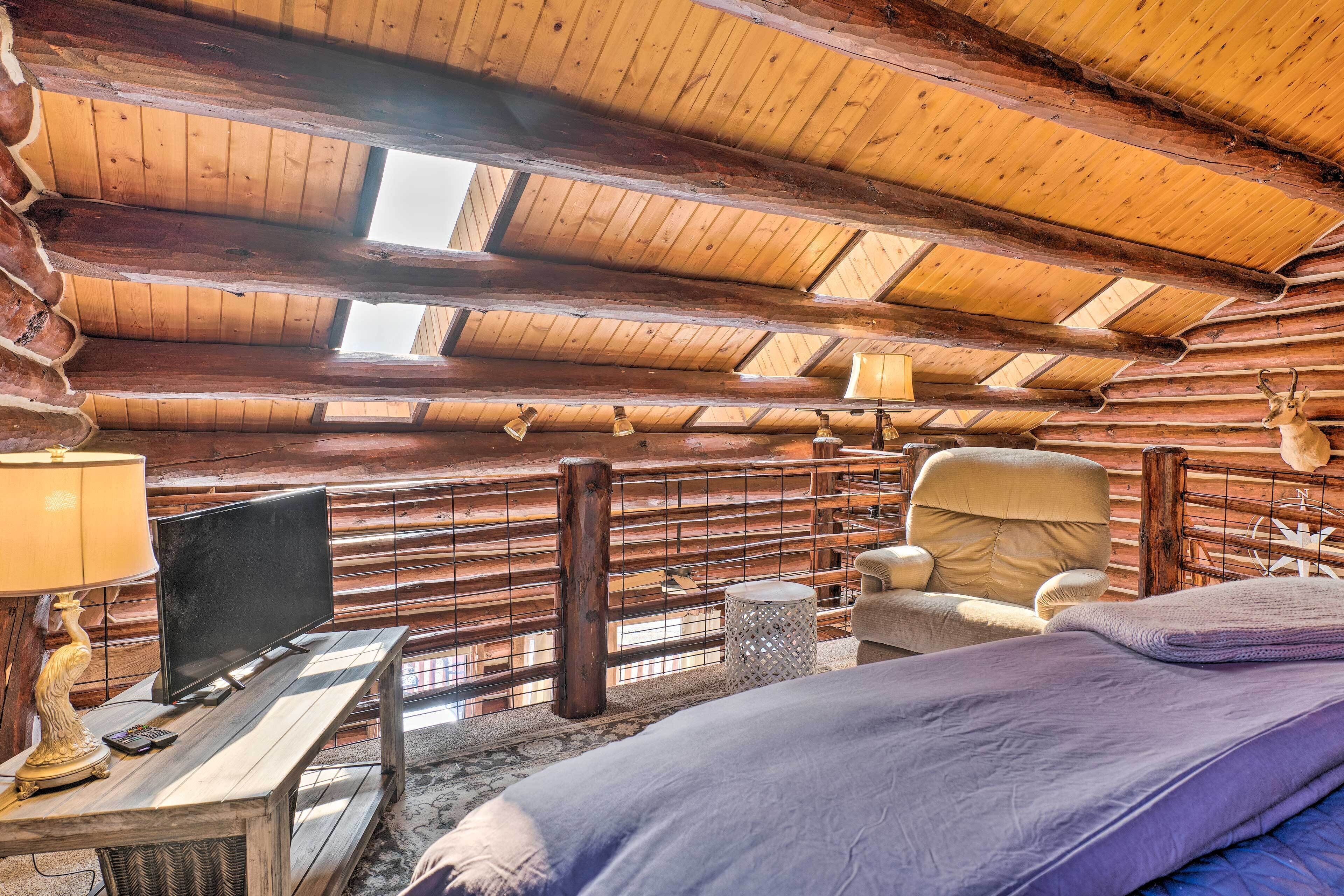 A log cabin room with a wooden ceiling, a bed, a chair, a television, and a lamp.
