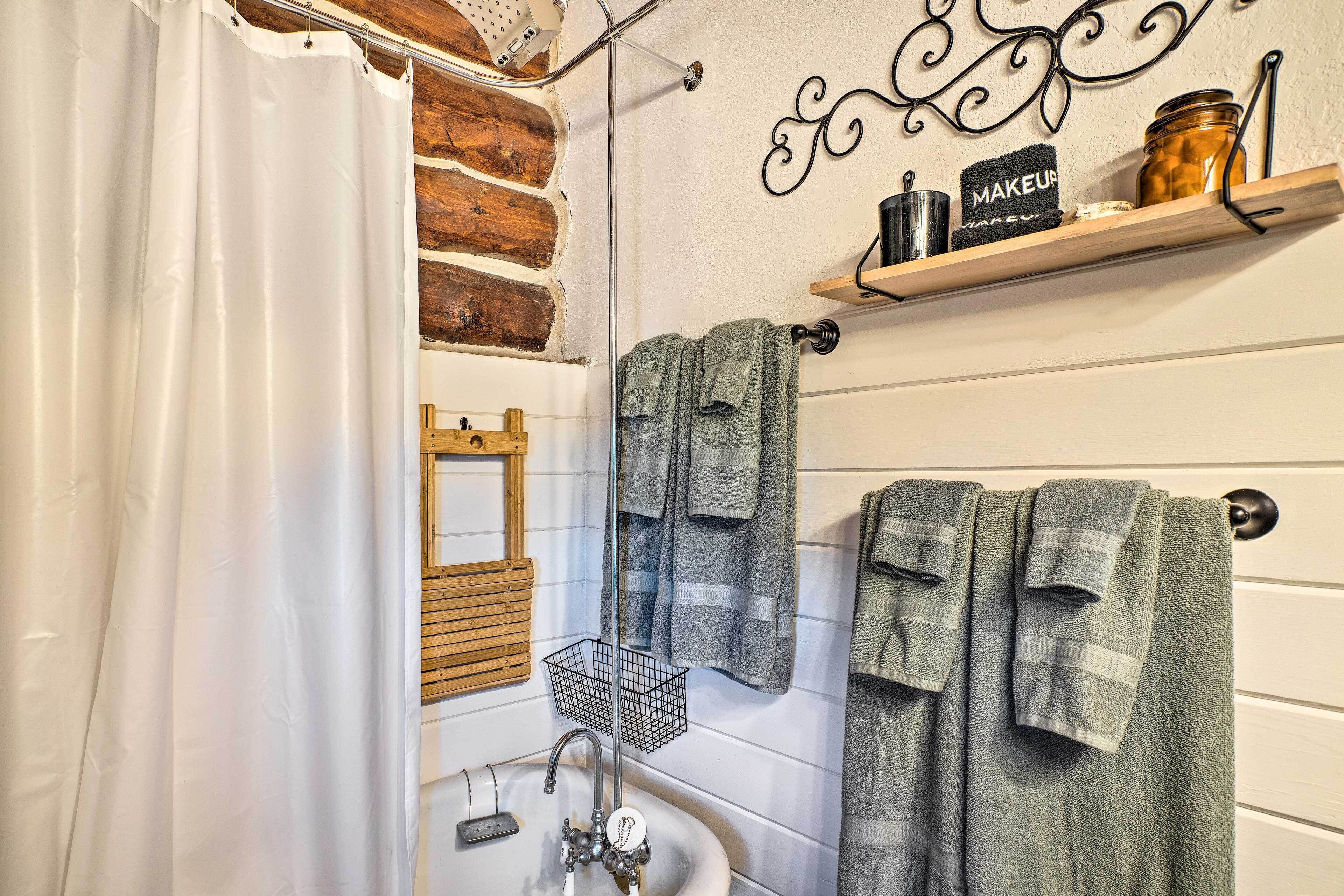 Casa de banho com lavatório branco, espelho, porta-toalhas e prateleira com um frasco e uma toalha com a inscrição 'MAKEUP'.