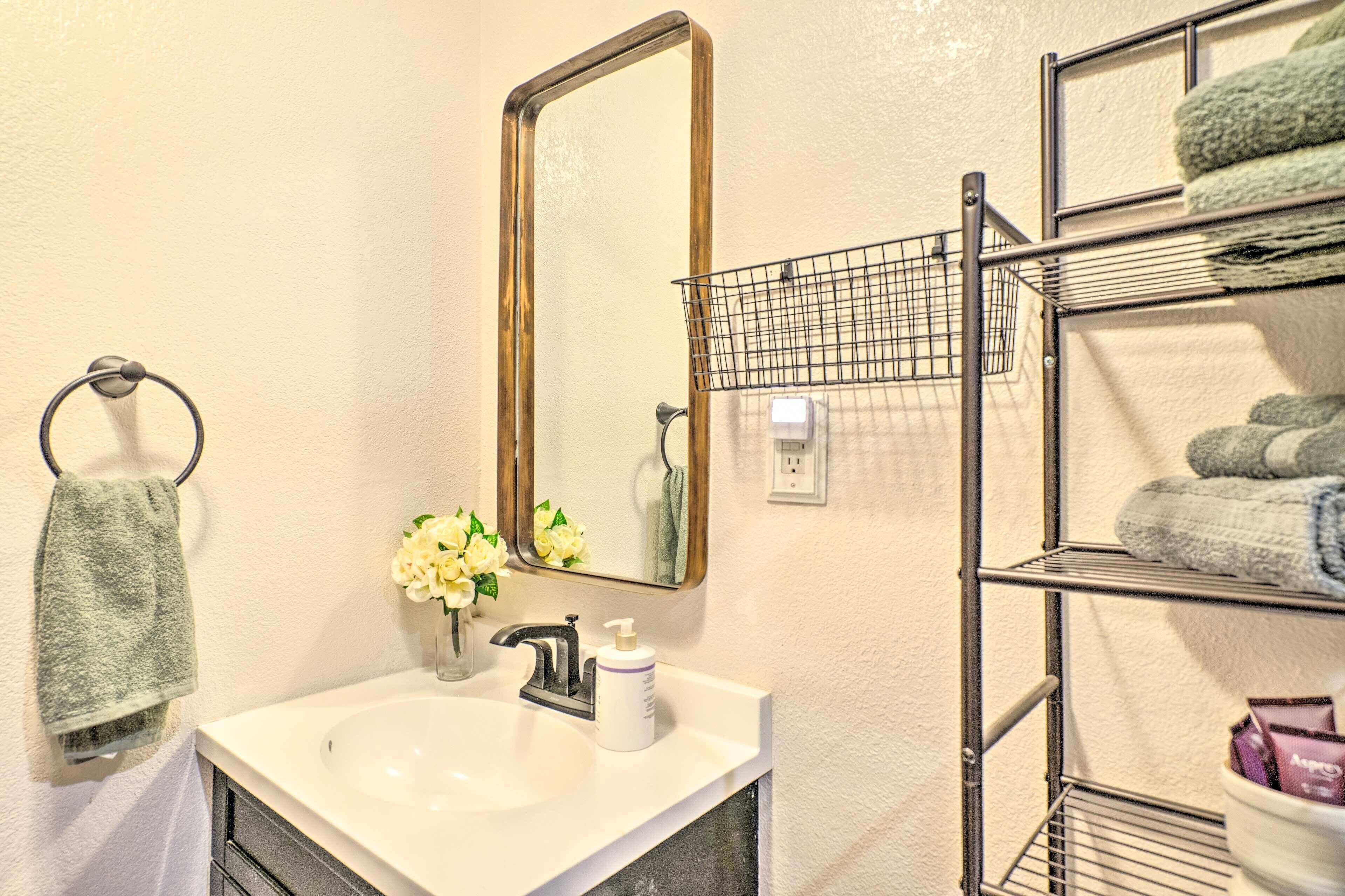 A bathroom with a sink, mirror, towel rack, and a shelf with folded towels.