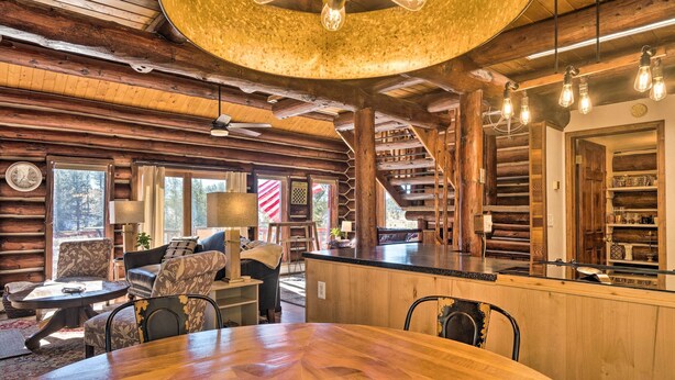 Interior de una cabaña de troncos con una mesa de comedor de madera, sillas, un sofá y una zona de bar.