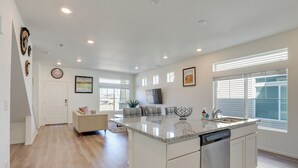 A modern kitchen with a large island, white cabinetry, and a dishwasher. There is a dining area with a sofa and a coffee table. - Colorado Retreat Near Hiking, Golfing & Fishing! (Commerce City)