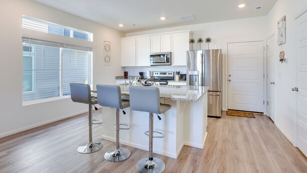 A modern kitchen with white cabinets, stainless steel appliances, and a bar area with stools. - Colorado Retreat Near Hiking, Golfing & Fishing! (Commerce City)