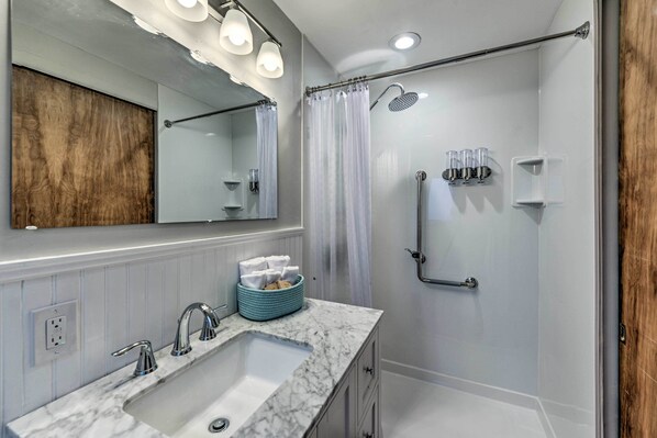 Un baño moderno con lavamanos de mármol, un espejo grande y una zona de ducha.