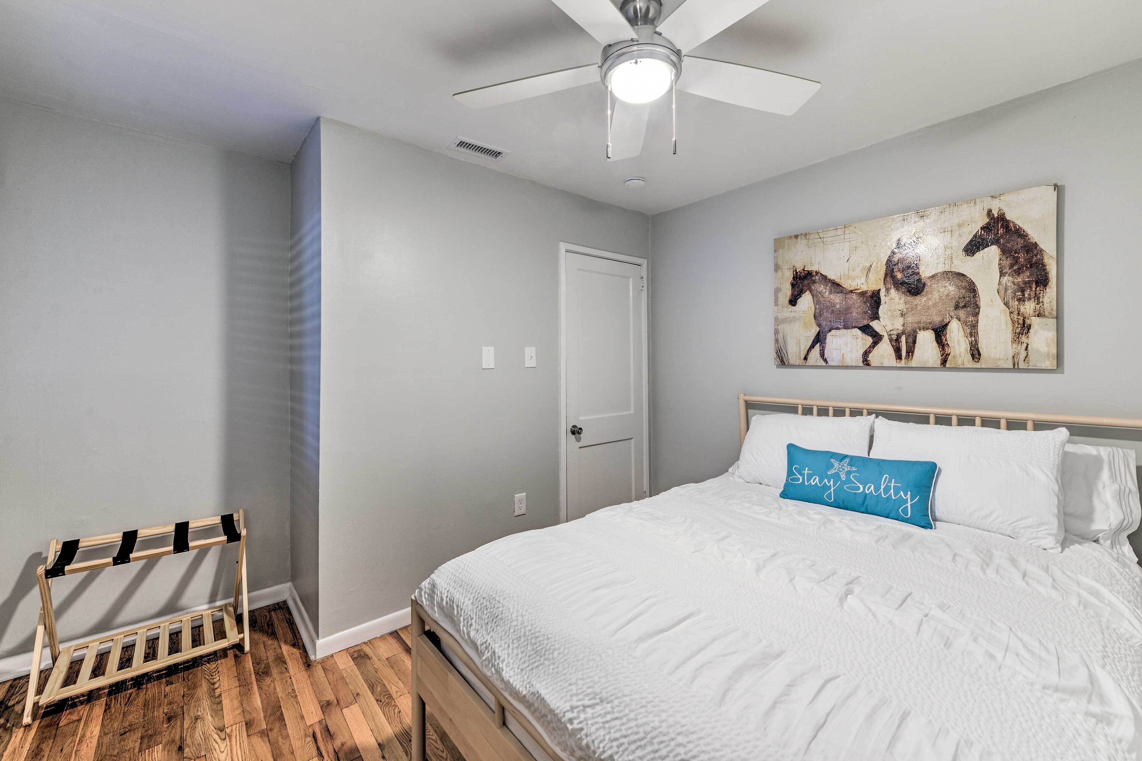 A bedroom with a bed, a ceiling fan, a wall-mounted horse painting, and a wooden rack.