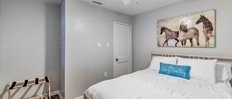 A bedroom with a bed, a ceiling fan, a wall-mounted horse painting, and a wooden rack.